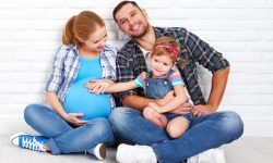 Happy family father and pregnant mother and child daughter near a blank brick wall in the room